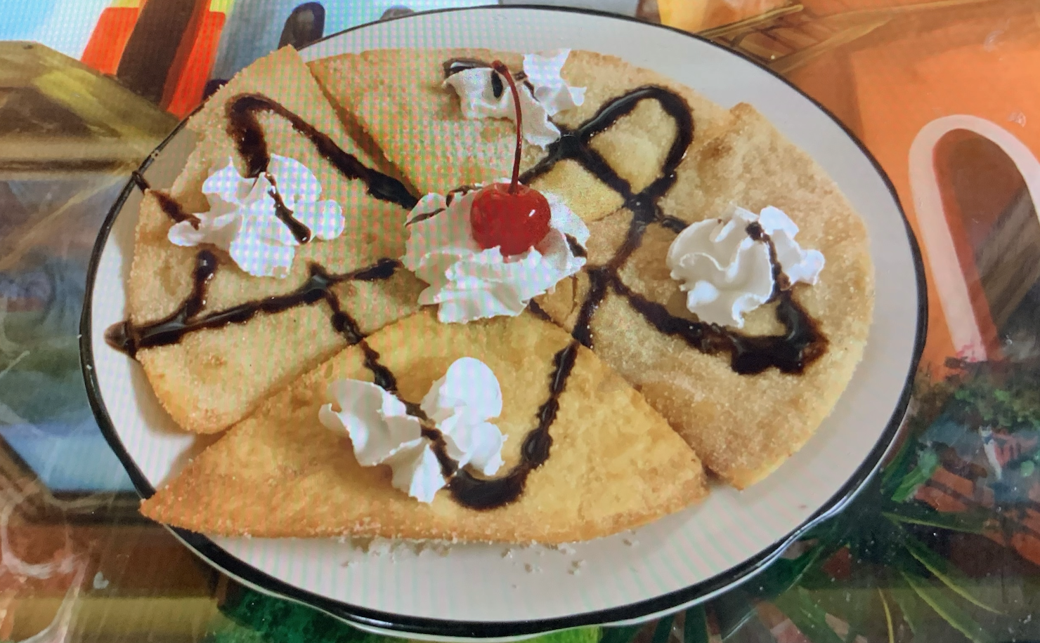 Golden fried sopapilla coated in sugar-cinnamon, topped with a maraschino cherry, drizzles of honey and chocolate, finished with a dab of whipped cream.